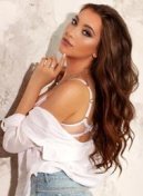 Evelina thumbnail - long wavy hair and white shirt against a stone wall