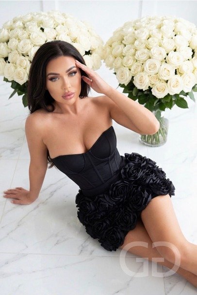 Sierra in a black strapless rose mini dress beside white roses