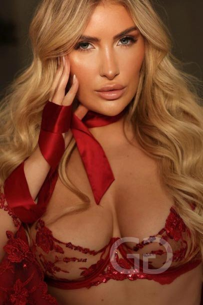 Nataly, busty London escort, in red embroidered lingerie with a red silk ribbon