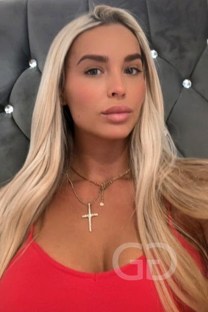 Lulu, blonde English escort in London, in a red top with a gold cross necklace